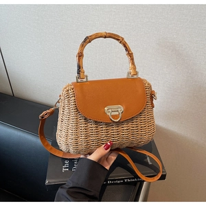 Close-up of woven straw handbag with bamboo handle, leather flap, and metal ring buckle