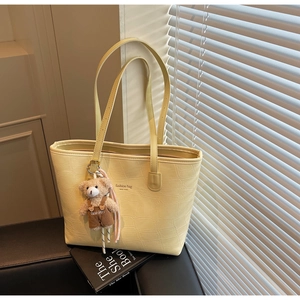 Detail of yellow crocodile embossed tote bag with teddy bear charm and fashion text