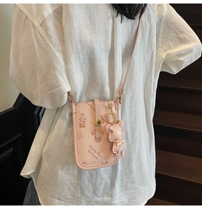 Pink crossbody phone bag with bear print and cute charm shown on a model for size scale