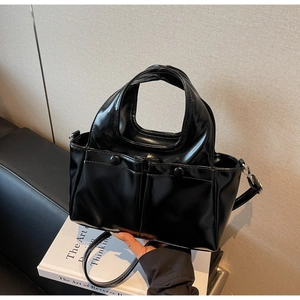Close-up of a glossy black patent leather tote bag with unique cut-out handle and pockets