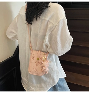 Pink crossbody phone bag with cartoon bear print and matching bear charm on model