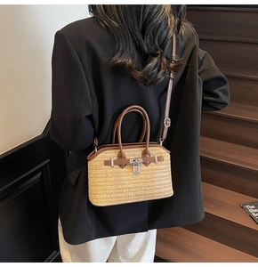 Detailed view of woven straw handbag with brown leather trim and silver metal lock on model