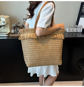 Detail of hand-woven straw tote with fringe trim and leather straps in a cafe setting