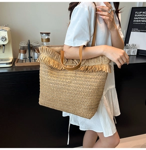 Detail of bohemian straw tote bag with decorative fringe and long brown handles