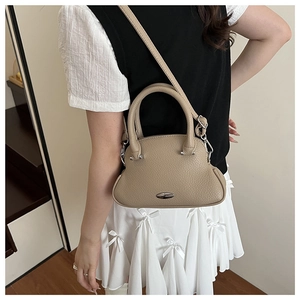 Detail of a beige pebbled leather handbag with silver oval plaque and adjustable strap