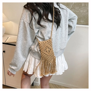 Detail of woven straw crossbody bag featuring boho tassels and diamond patterns