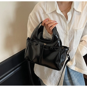 Detail of a black glossy tote bag with shiny finish, dual handles, and silver metal hardware