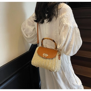 Detail of hand-woven straw bag with bamboo handle and brown leather flap closure