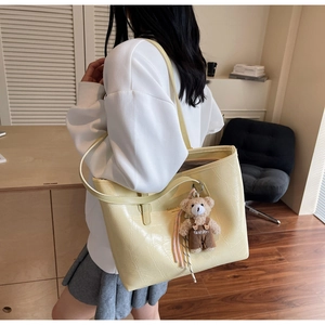 Close-up of pale yellow crocodile texture tote bag with plush bear charm and gold lettering