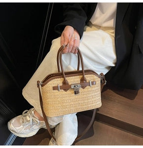 Detail of straw handbag with dark brown leather trim and metallic lock on crossbody strap