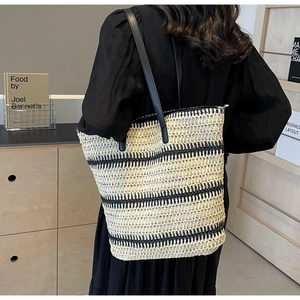 Détail d'un grand sac cabas tissé avec des rayures noires et beige et anses en cuir