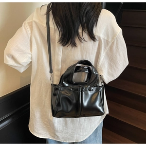 Detail of a black glossy patent leather mini tote bag with dual front button pockets
