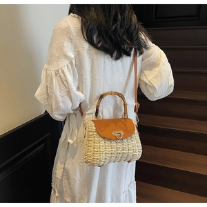 Straw handbag with bamboo handle and leather strap worn by a model on wooden stairs