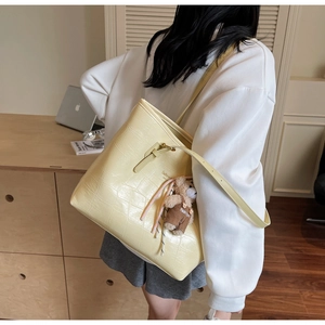 Detail of yellow crocodile embossed tote bag with teddy bear charm and fashion text