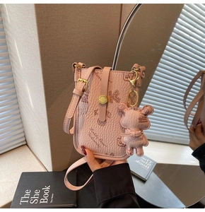 Close-up of pink crossbody phone bag with bear pendant and textured leather detail