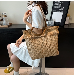 Detail of hand-woven straw tote bag featuring brown faux leather handles and fringe trim