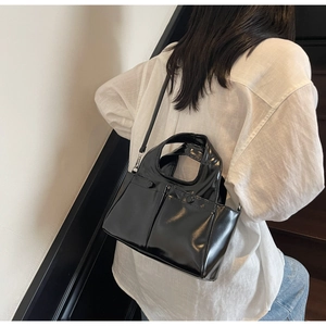 Model wearing a black glossy tote bag with circular handles on a white shirt background