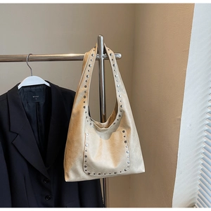 Gros plan du sac cabas en cuir beige avec clous argentés suspendu à côté d'un blazer