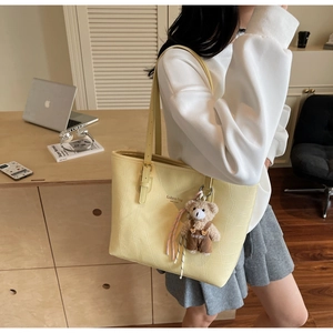 Detail of yellow crocodile pattern tote bag with teddy bear pendant and fashion text