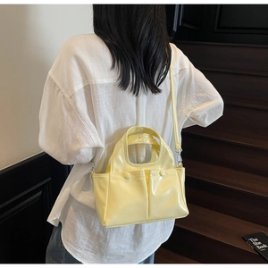 Rear view of model wearing a light yellow patent leather tote bag on wooden stairs