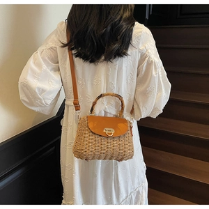 Detail of woven straw crossbody bag featuring bamboo handle and brown leather flap