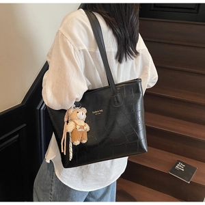 Detail of black crocodile pattern tote bag with cute bear pendant and printed text