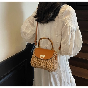 Detailed view of woven straw bag with bamboo handle and leather flap on a model