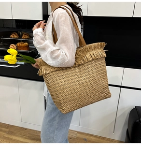 Detail of woven straw tote bag featuring decorative fringe and brown leather straps