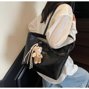 Detail of black crocodile embossed tote bag with gold logo and cute bear charm pendant