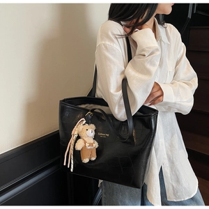 Detail of black faux crocodile tote bag with cute bear charm and gold New York lettering