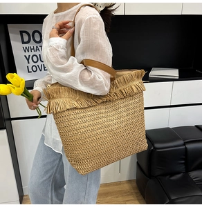 Detail of a beige woven tote bag with fringe edge and brown leather strap on model