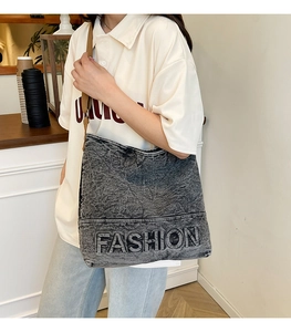 Detail of black denim tote bag with FASHION embossed logo and adjustable brown strap