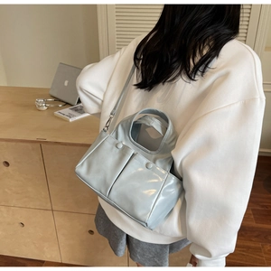 Detailed view of a light blue glossy leather tote bag worn as a crossbody shoulder bag
