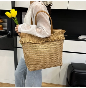 Straw tote bag with brown handles and fringe detail shown in a modern lifestyle setting
