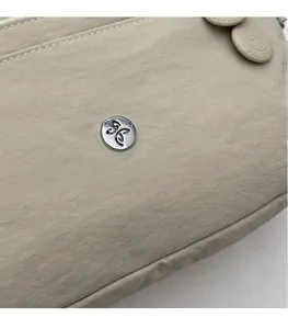 Gros plan d'un sac bandoulière en nylon beige avec logo argenté rond et texture plissée