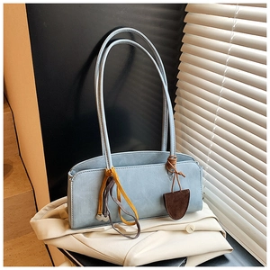 Détail d'un sac baguette bleu clair minimaliste avec lanières sur fond de blazer