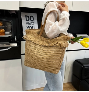 Detail of hand-woven straw tote bag with fringe edge and long shoulder strap in use
