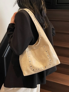 Sac fourre-tout beige à rivets argentés avec texture cuir porté par un mannequin