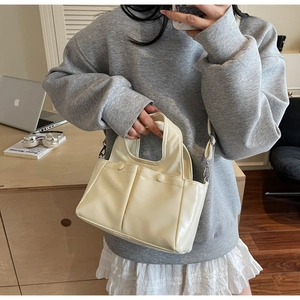 Close-up of creamy white tote bag featuring dual front buckle pockets and matte texture