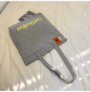 Détail du sac cabas en nylon gris avec texte jaune et écusson chat orange brodé