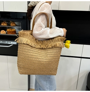 Close-up of woven straw tote bag with fringe edge and premium brown leather handles