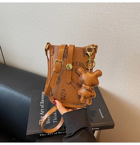 Detail of brown litchi leather mini bag featuring a teddy bear print and matching bear charm