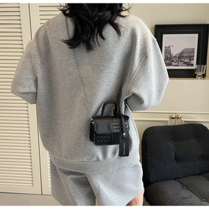 Detail of black mini crossbody bag with leather texture, chain strap, and fashion tag