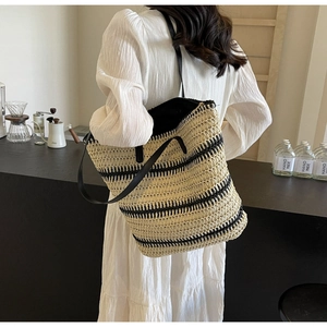 Détail d'un sac cabas tissé avec rayures noires et bandoulière en cuir sur modèle