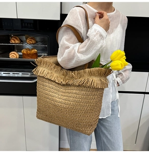 Detail of hand-woven straw tote bag with brown leather strap and decorative tassels