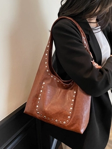 Sac bandoulière en similicuir marron à clous porté par un mannequin en costume noir