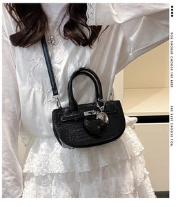 Model wearing black faux crocodile handbag with metallic heart charm and slim strap