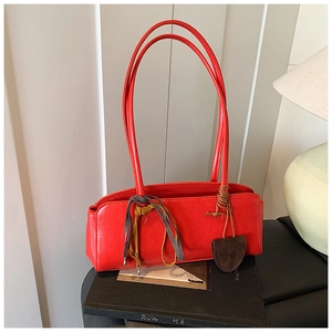 Détail du sac bowling rouge verni avec ruban en soie et pendentif cœur posé sur un livre