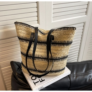Détail d'un grand sac cabas en paille avec rayures noires et bandoulières en cuir
