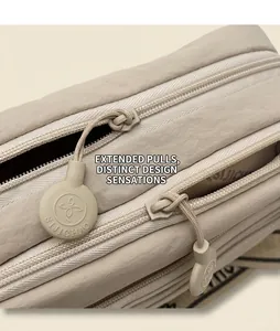 Détail de la tirette de fermeture ronde sur un sac bandoulière beige multicouche